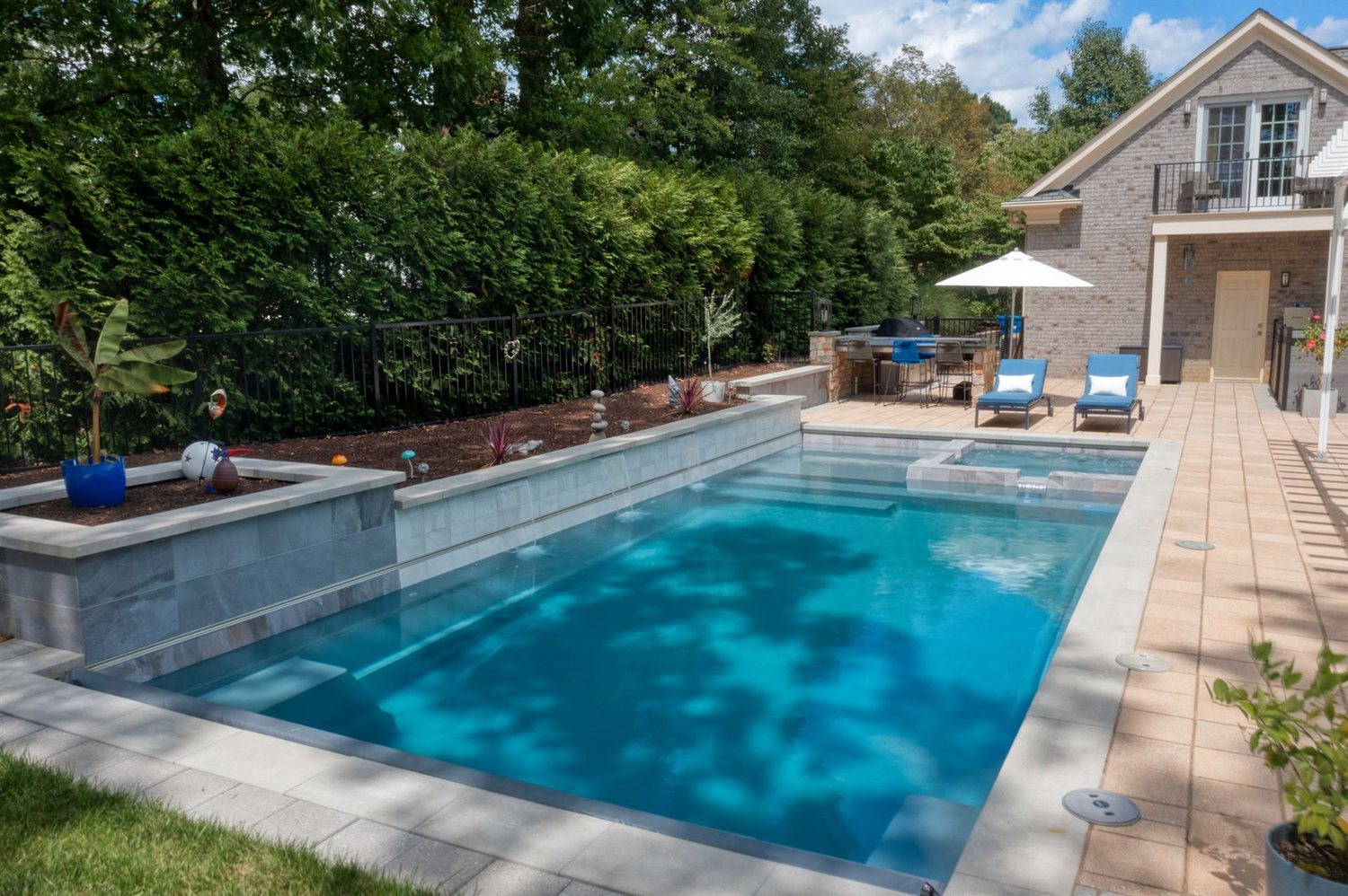 A finished fiberglass pool with raised spa, stone coping and paver patio
